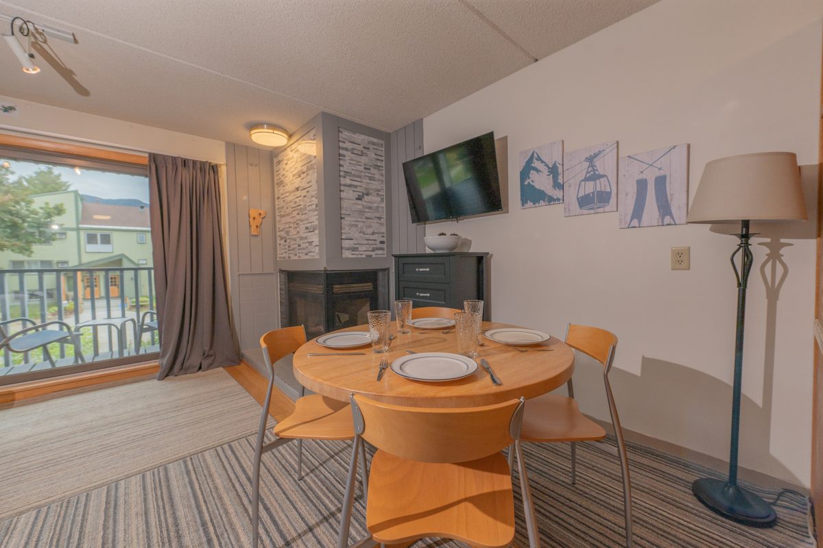 Round dining table beside the gas fireplace at Ski Stash Smuggs, with a wall-mounted TV and ski artwork