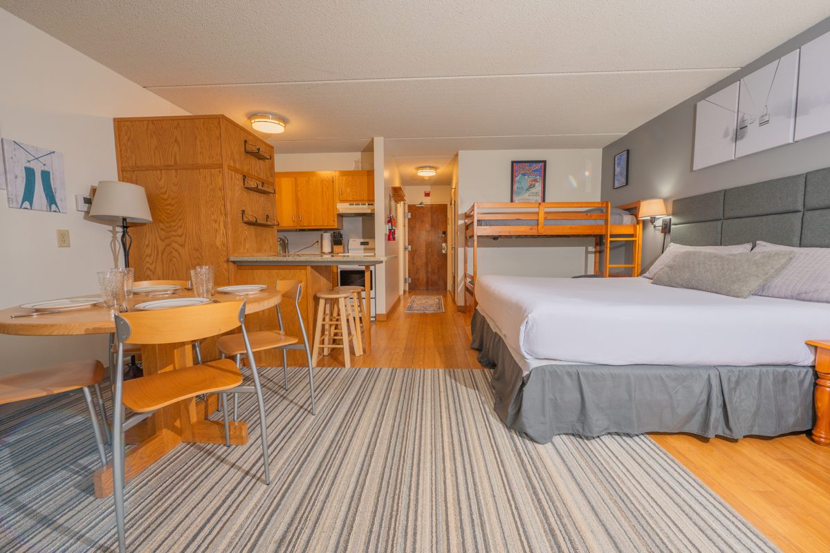 Full view of the open-plan studio at Ski Stash Smuggs showing the king bed, twin bunk beds, kitchen and entry